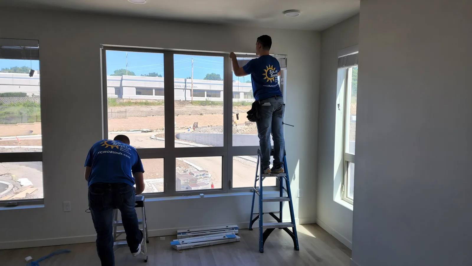 Two Solar Shield Blinds installers fitting blinds on a large window