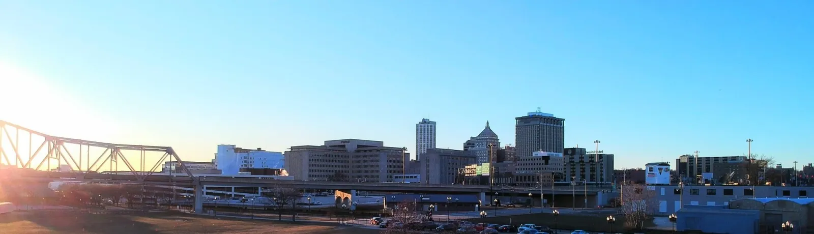 A panoramic view of a city skyline and river bridge at sunset