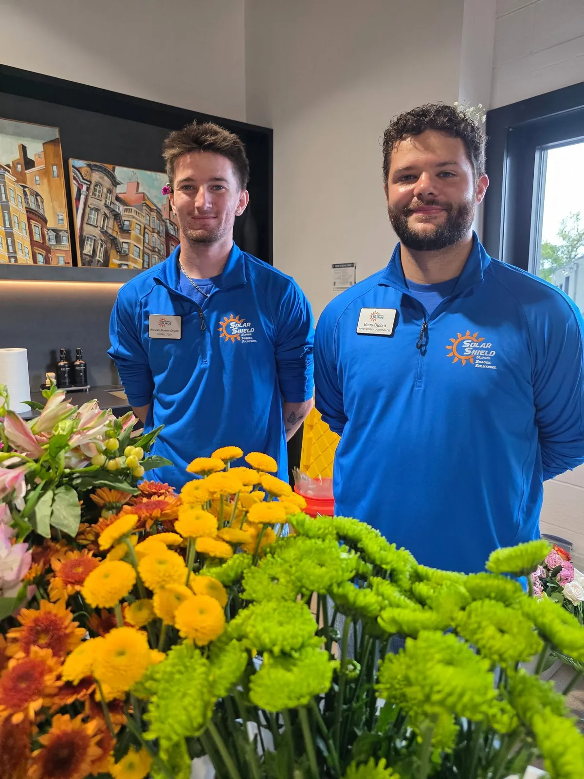 Two team members at an event beside a display of flowers