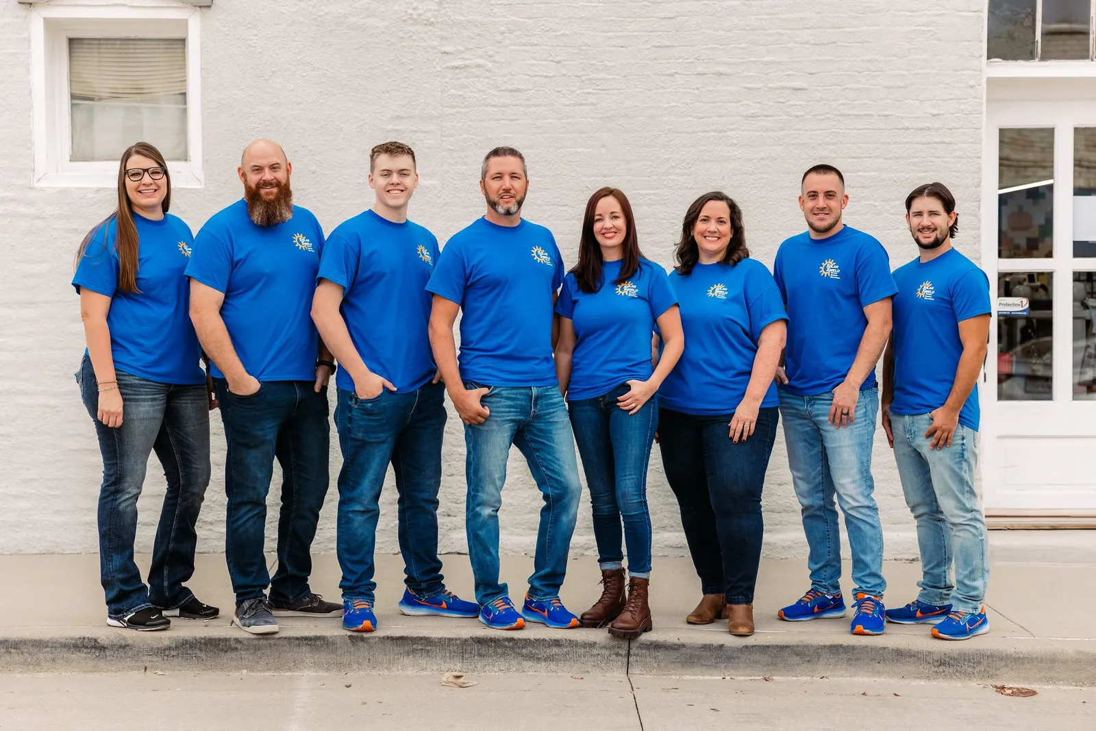 The Solar Shield Blinds team lined up in blue company shirts against a white wall