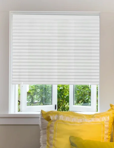 A white temporary shade installed on a window above yellow pillows