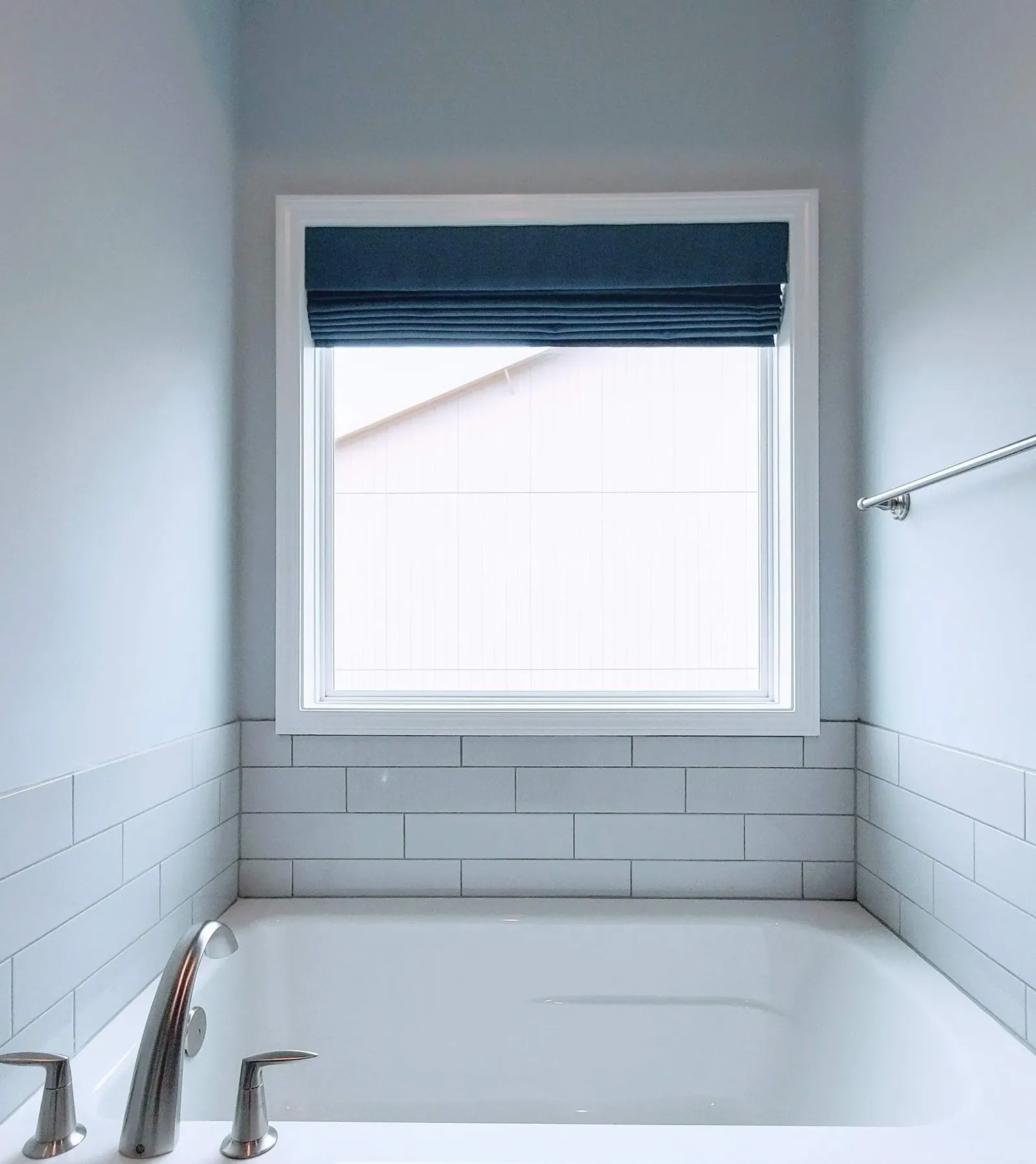 Navy Roman shade raised above a bathroom tub, installed by Solar Shield Blinds