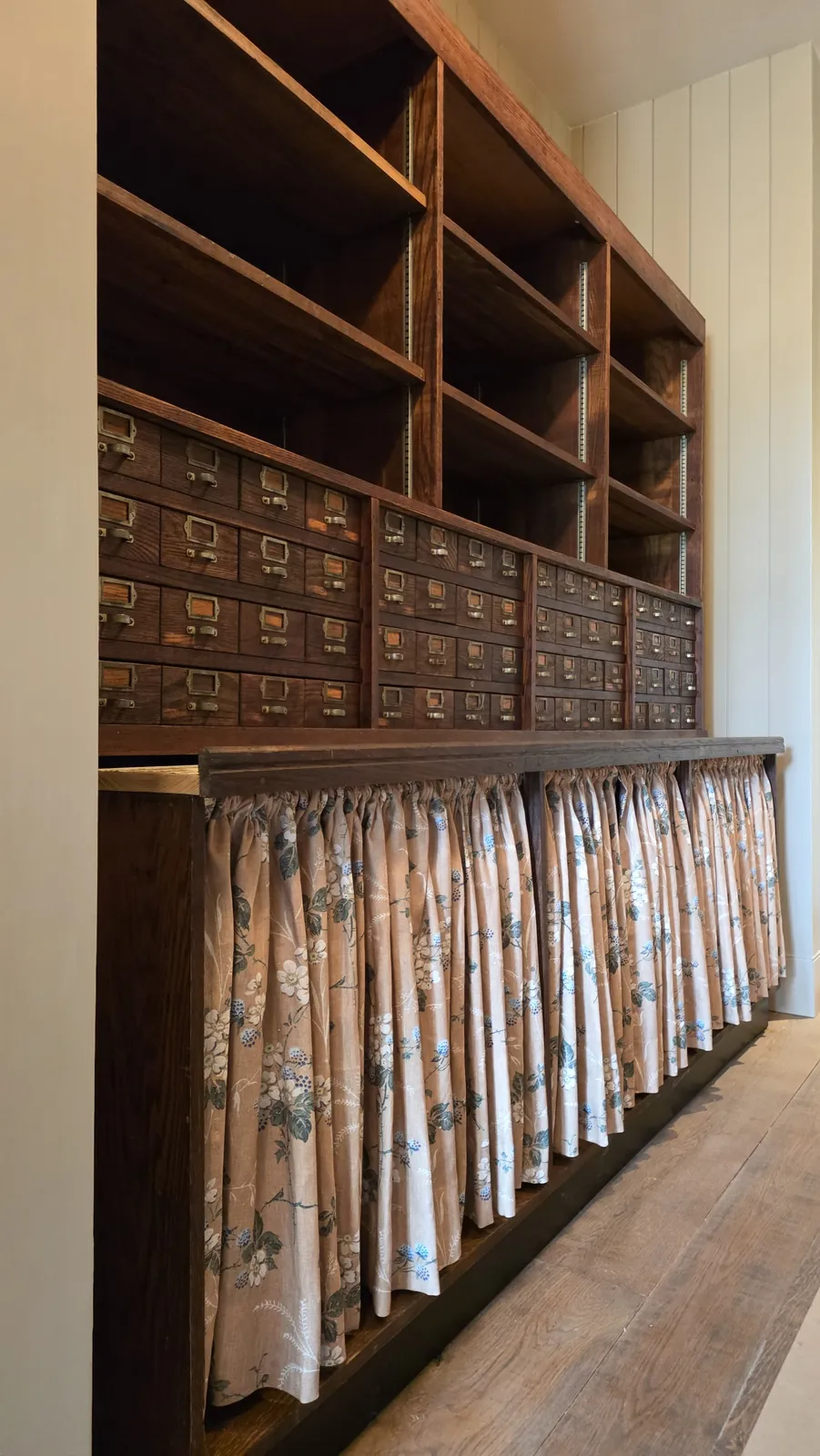 Floral cabinet curtains under wood apothecary drawers and open shelves, installed by Solar Shield Blinds