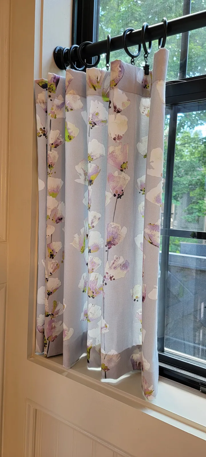 Close up of a floral café curtain hung on a black iron rod, installed by Solar Shield Blinds