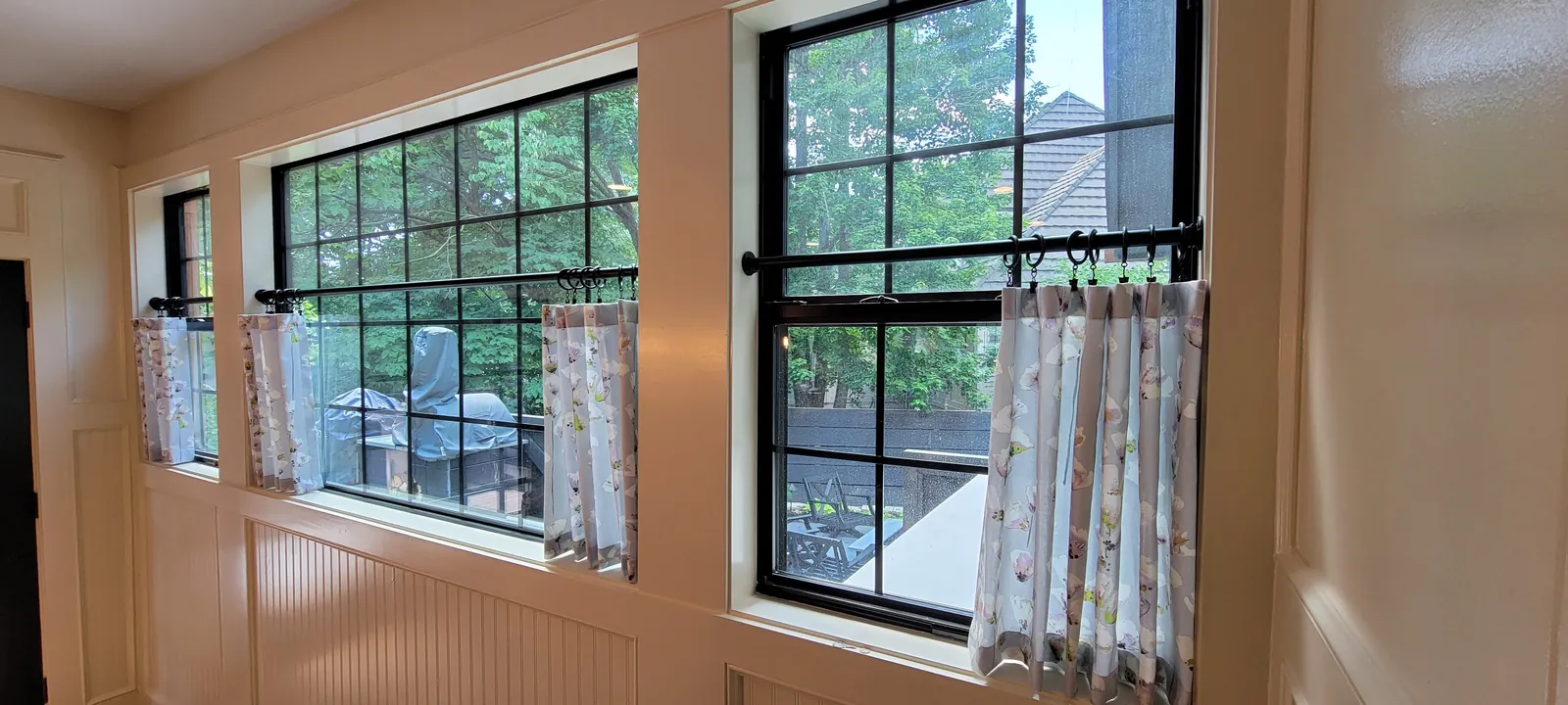 Floral café curtains across the lower half of a row of black framed windows, installed by Solar Shield Blinds