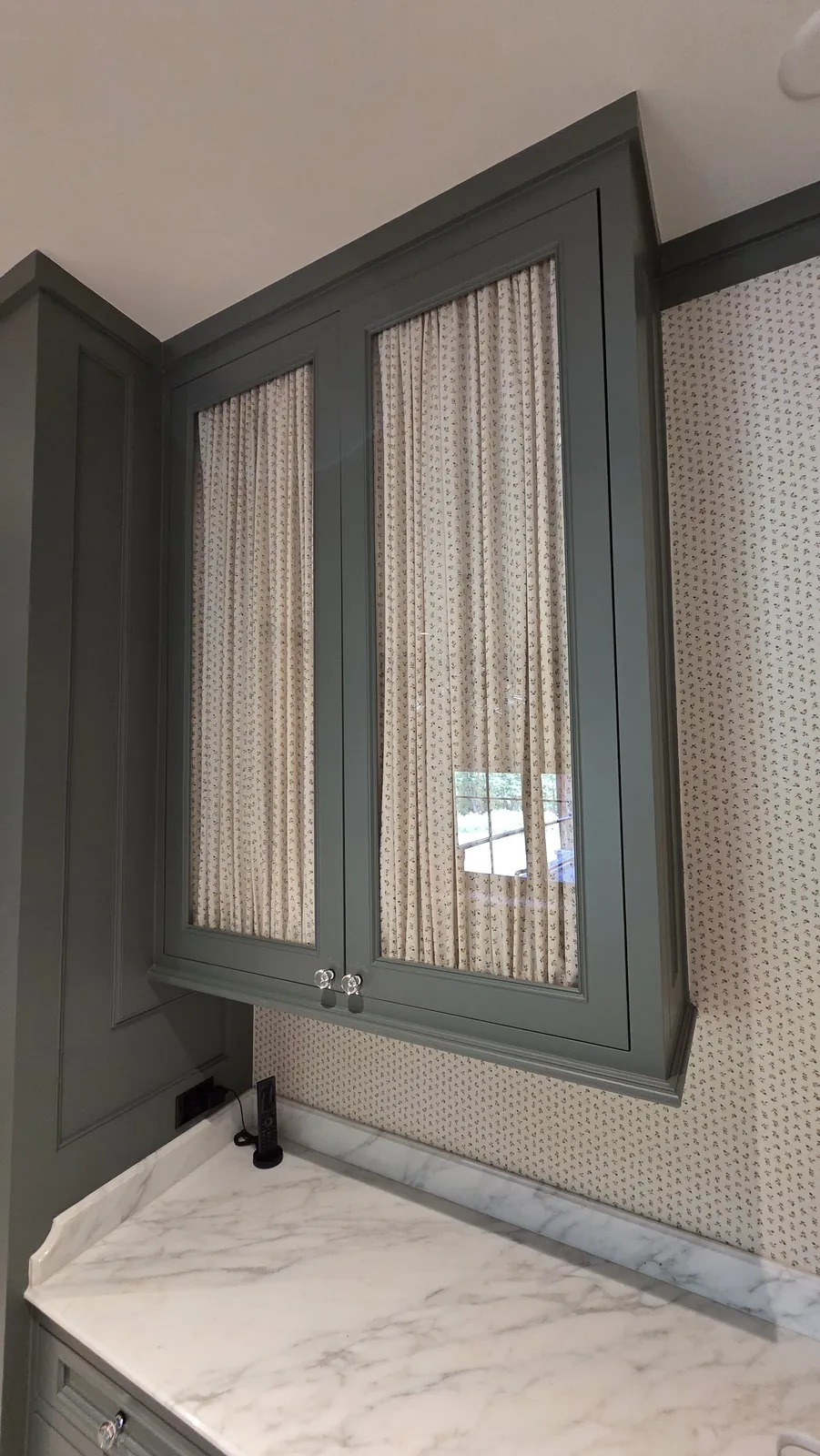 Striped curtains behind the glass doors of green upper cabinets, installed by Solar Shield Blinds