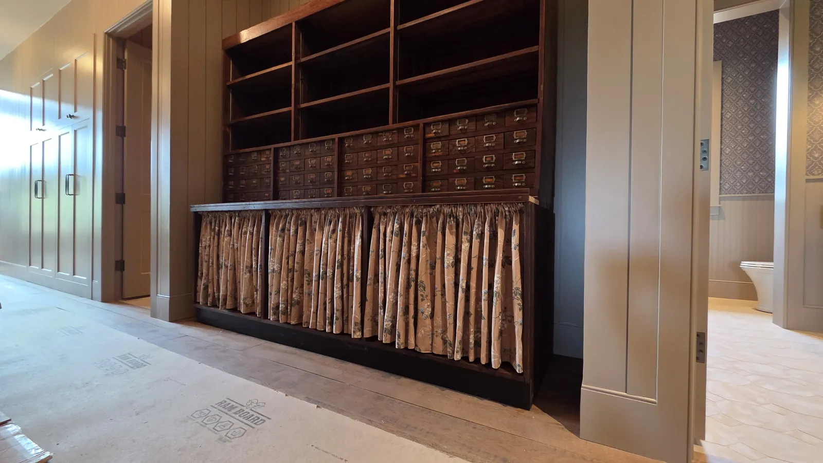 Gathered curtains covering the open shelving under a wall of apothecary drawers, installed by Solar Shield Blinds