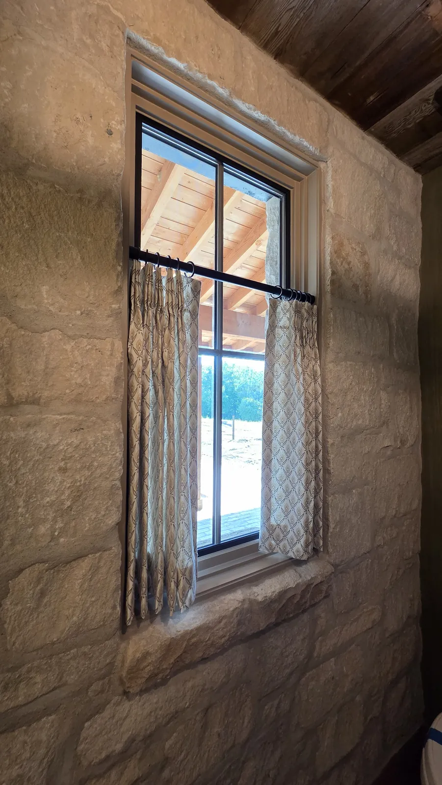 Café curtains on a window set into a stone wall, installed by Solar Shield Blinds