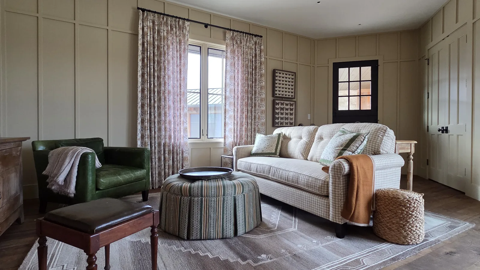 Floral drapery panels on the windows of a paneled living room, installed by Solar Shield Blinds