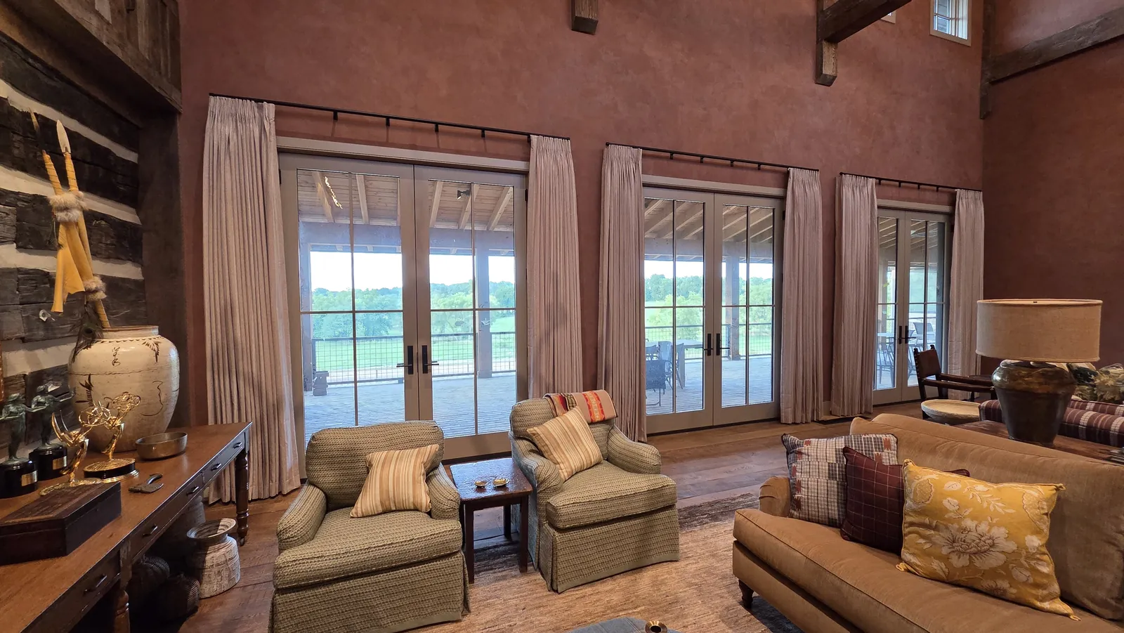 Drapery panels between the French doors of a great room with a log wall, installed by Solar Shield Blinds