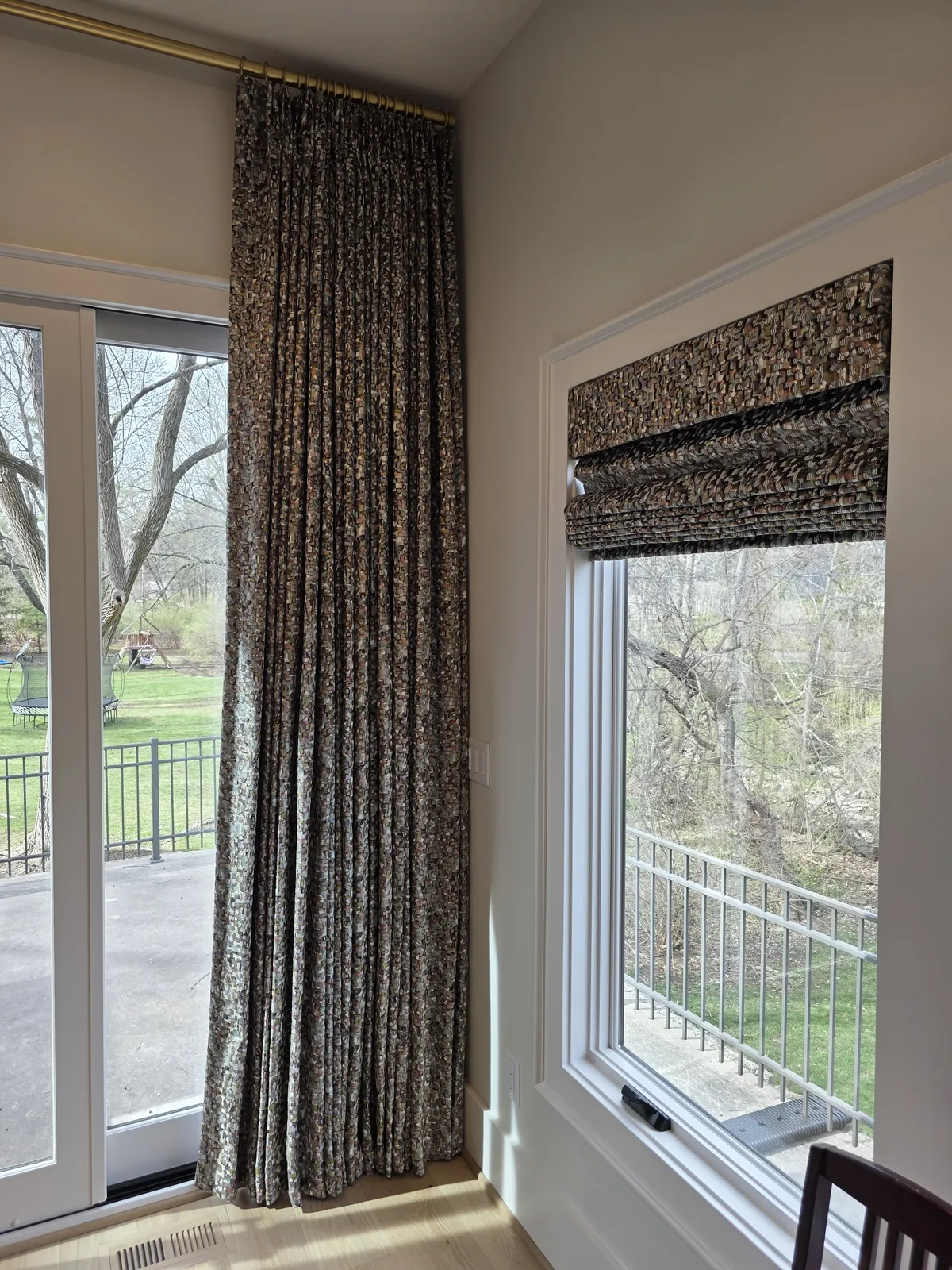 A patterned drapery panel beside a matching Roman shade on a patio door wall, installed by Solar Shield Blinds