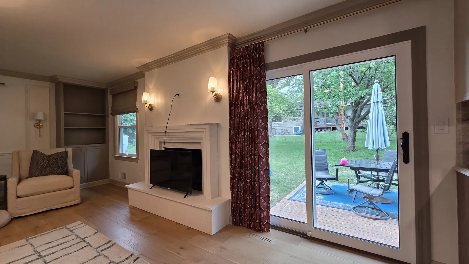 A deep red drapery panel beside a sliding patio door in a family room, installed by Solar Shield Blinds