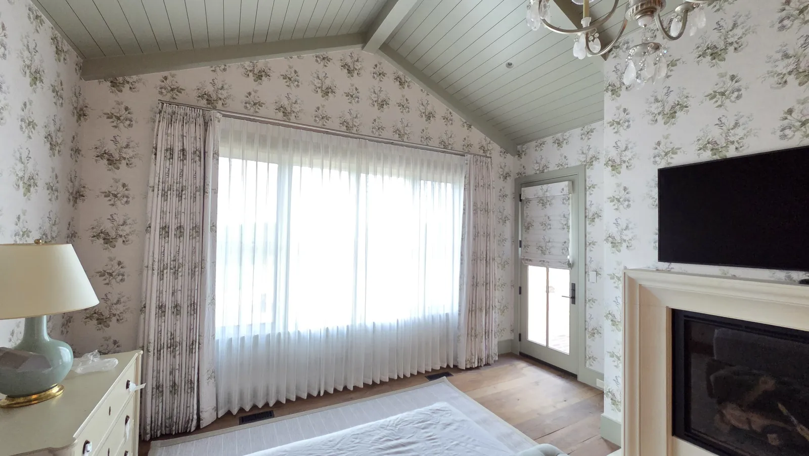 Sheer drapery panels across a wide window in a wallpapered sitting room, installed by Solar Shield Blinds