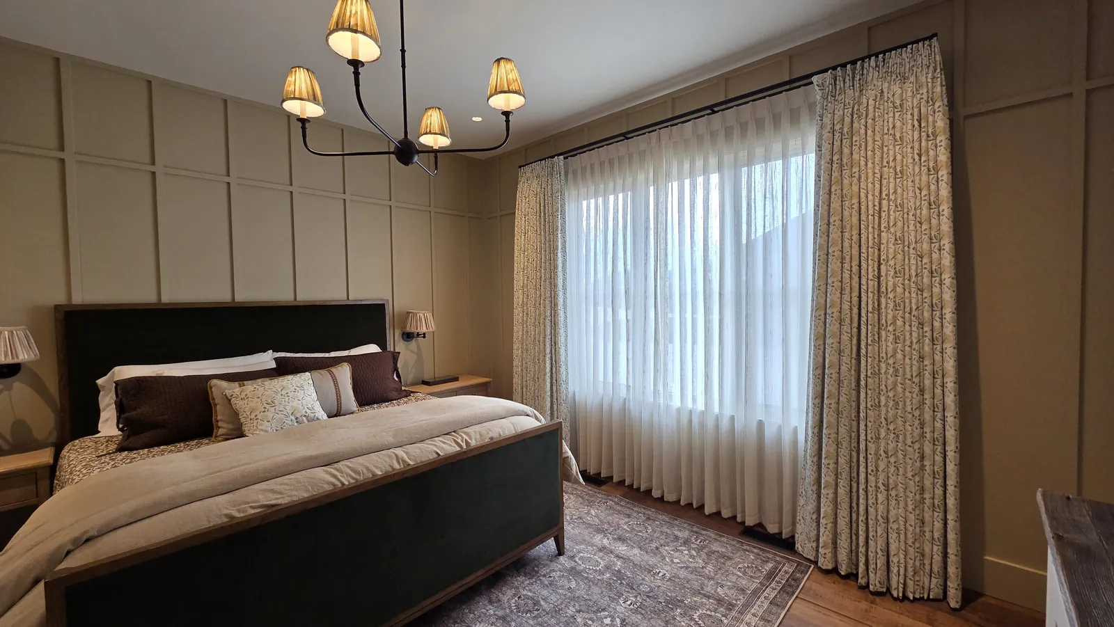 Sheer drapery across the windows of a primary bedroom with paneled walls, installed by Solar Shield Blinds