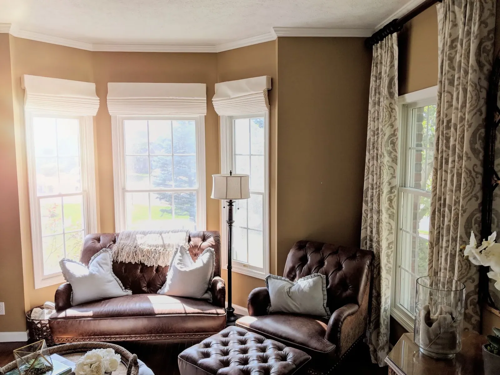 Custom drapery panels and Roman shades on living room bay windows, installed by Solar Shield Blinds