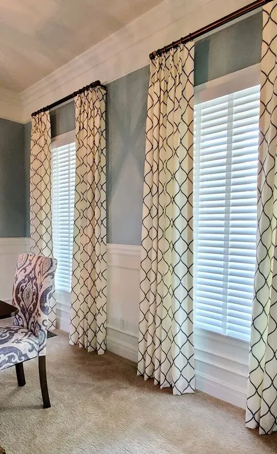 Patterned drapery panels beside plantation shutters, installed by Solar Shield Blinds