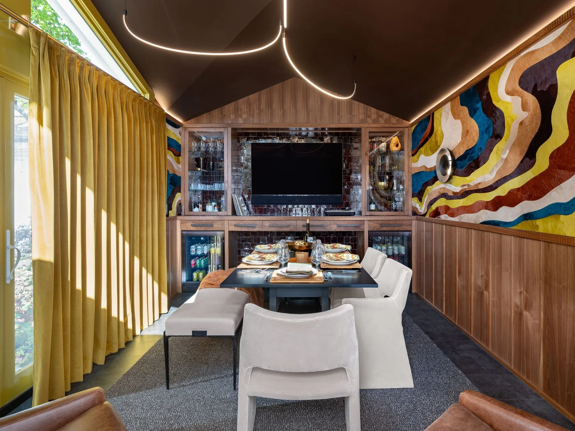 A dining room with mustard velvet drapery panels by Solar Shield Blinds, walnut millwork and a wavy cowhide mural