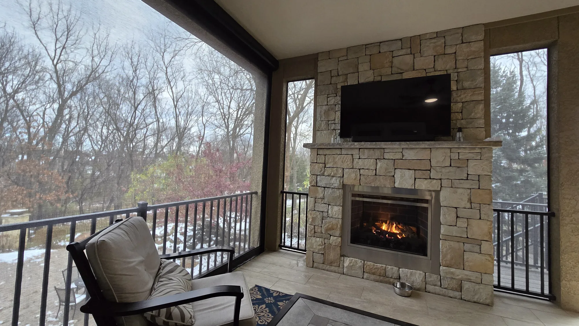 Exterior Patio Shades on a covered porch with a stone fireplace in winter, installed by Solar Shield Blinds