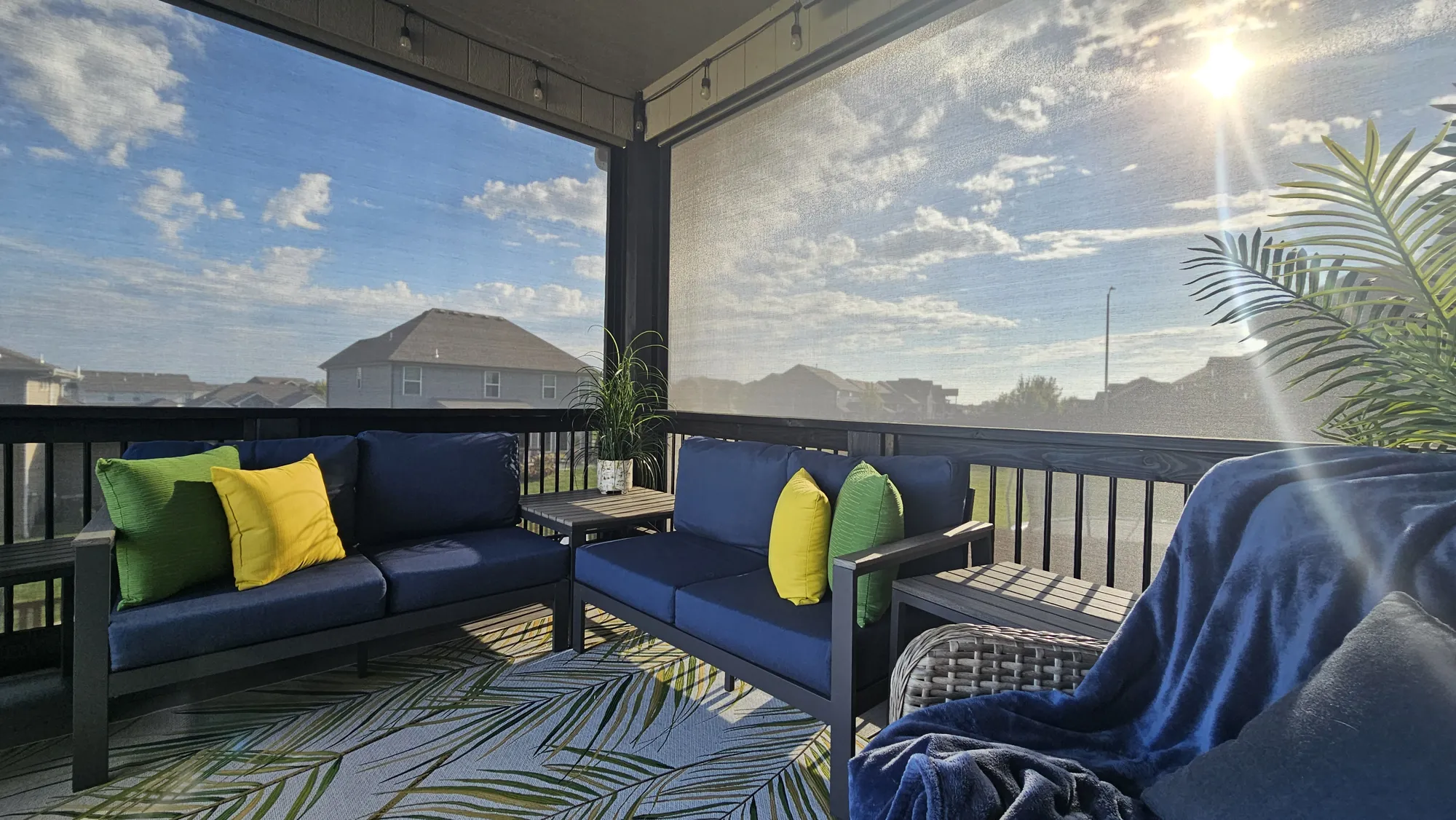 Exterior Patio Shades lowered against the sun on a covered deck with navy seating, installed by Solar Shield Blinds