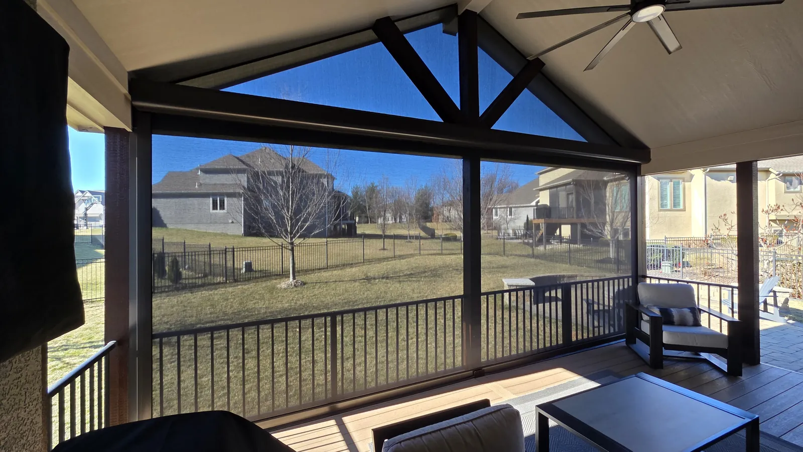A screened deck under a gable with timber trusses, looking out to the back yard