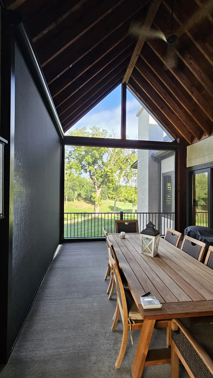 Inside a screened patio with a long wood dining table, the gable triangle screened above