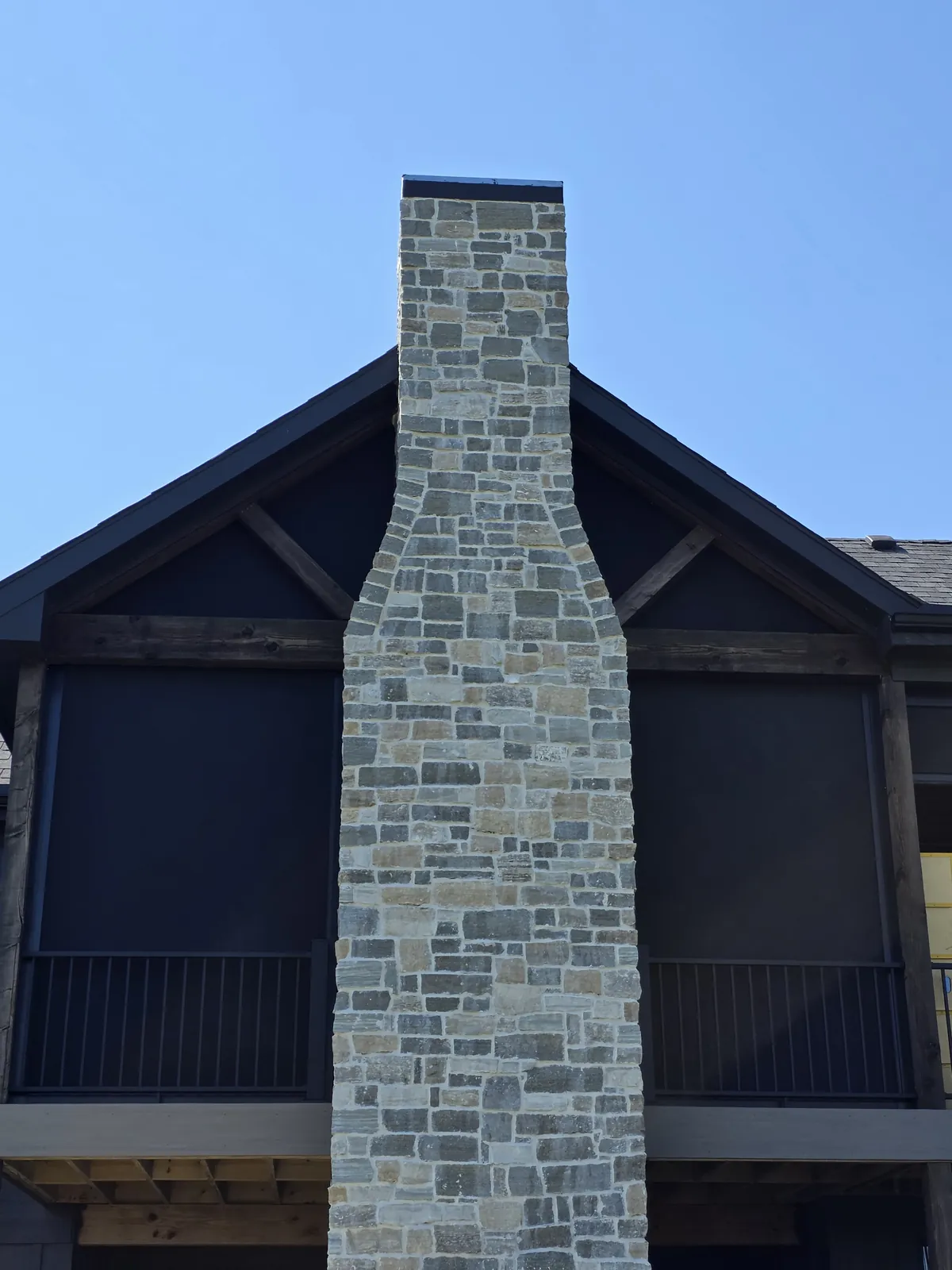 A stone chimney rising between screened porches on the back of a dark home