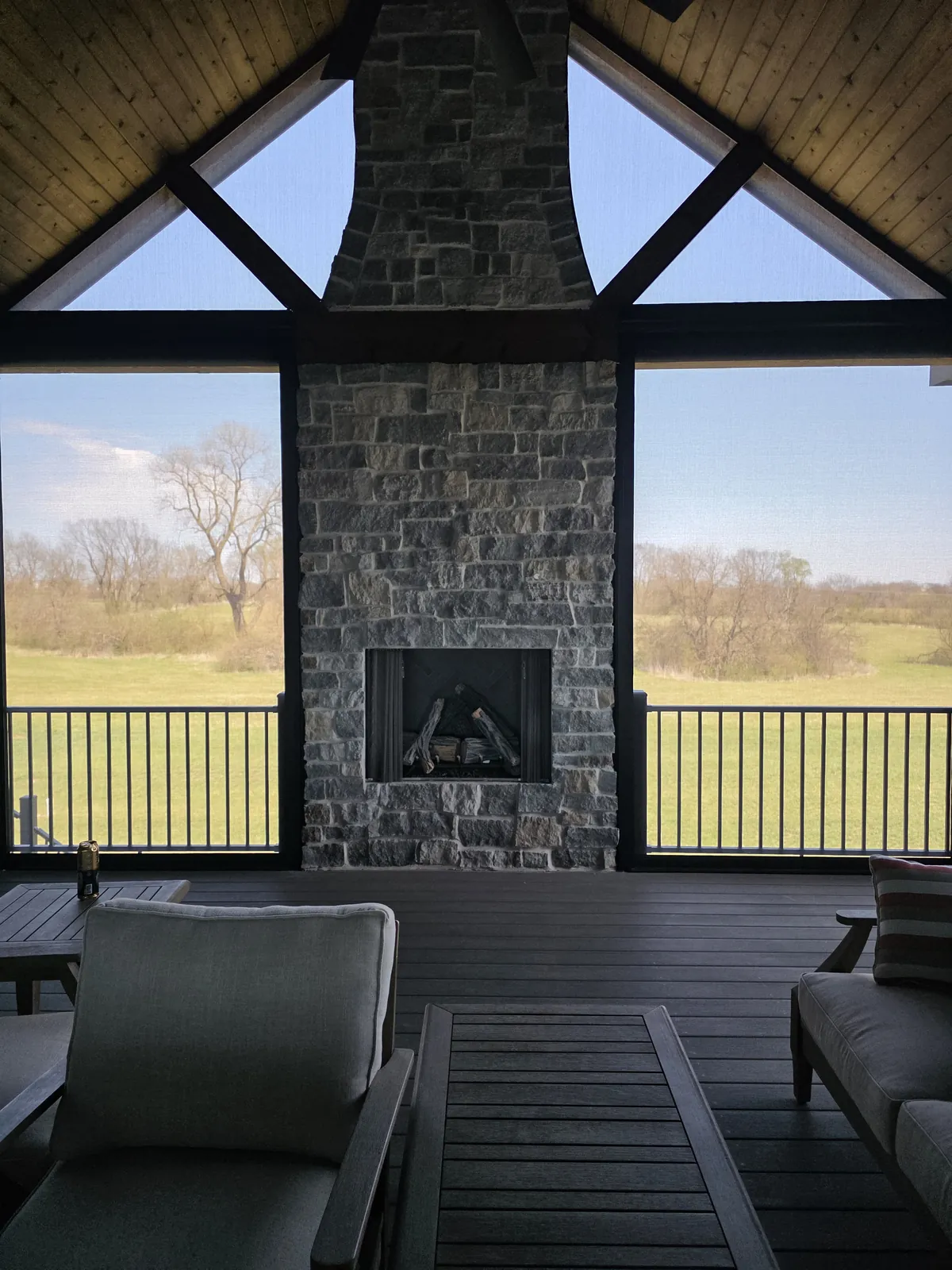 A screened porch with a stone fireplace, fixed screens in the angled openings either side of the chimney