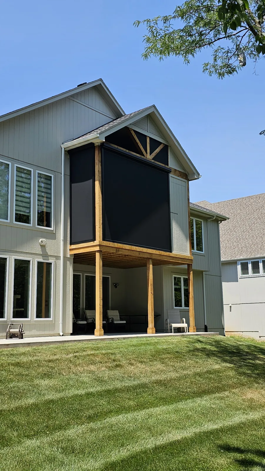 A screened upper deck under a gable on a gray two story home, above an open lower patio