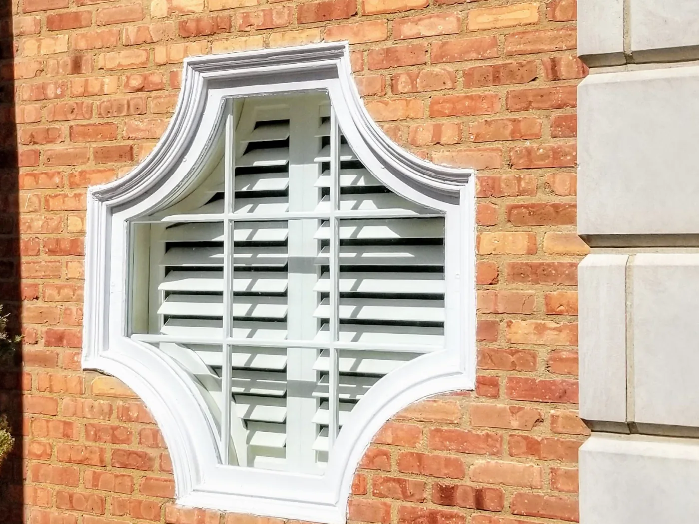 The handcrafted cross-pattern arched window seen from outside, shutters fitted inside it