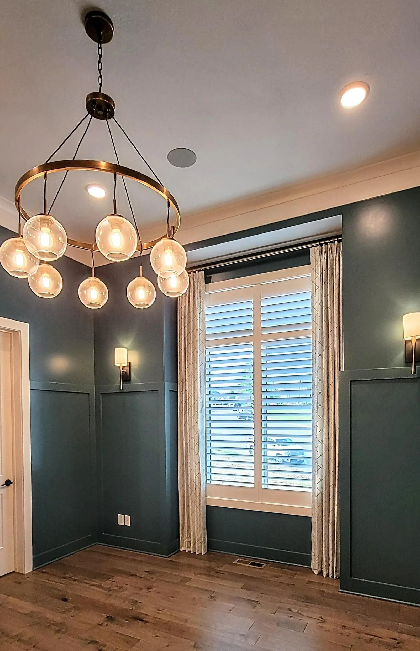 Plantation shutters and drapery panels in a dining room with a chandelier
