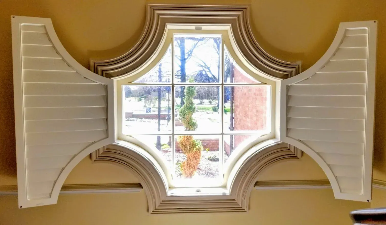 Custom plantation shutter panels opened back from the cross pattern window