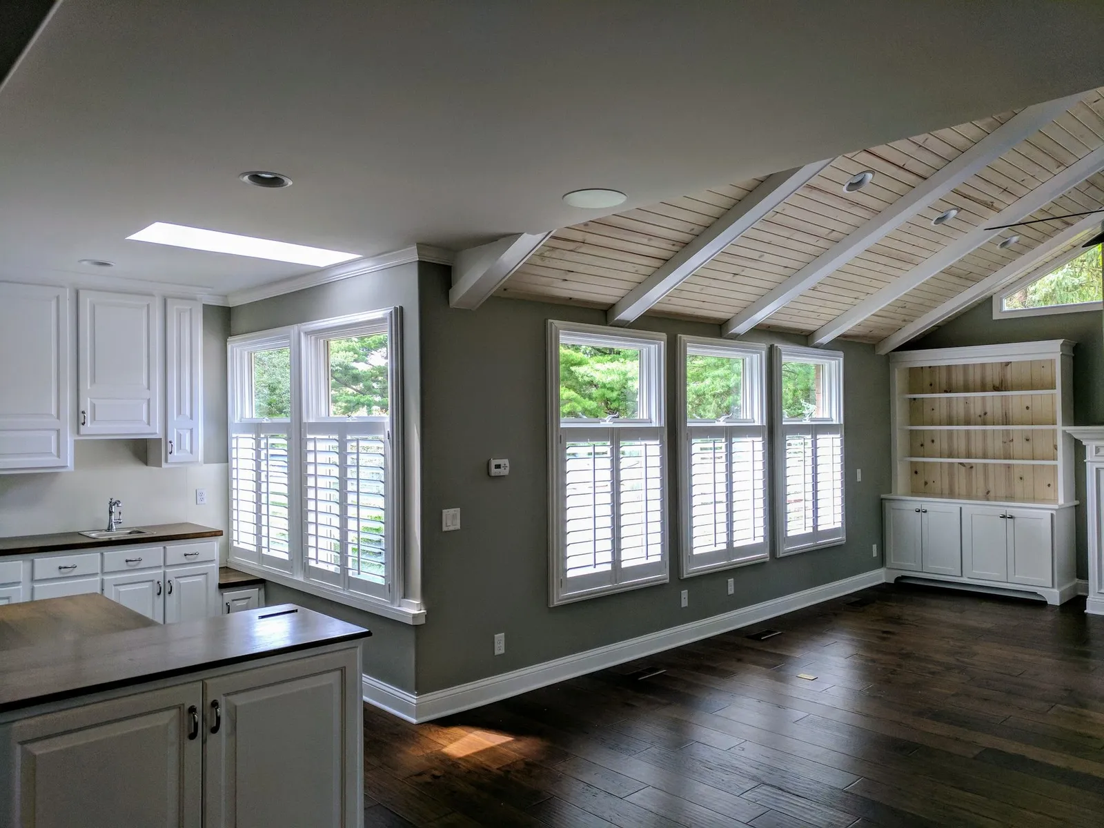 White plantation shutters on the windows of an open kitchen and family room with a vaulted ceiling