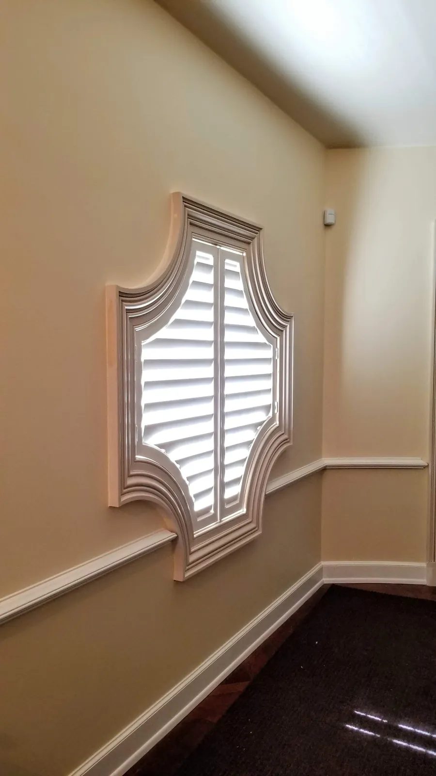A custom plantation shutter fitted to a specialty shaped window in a hallway