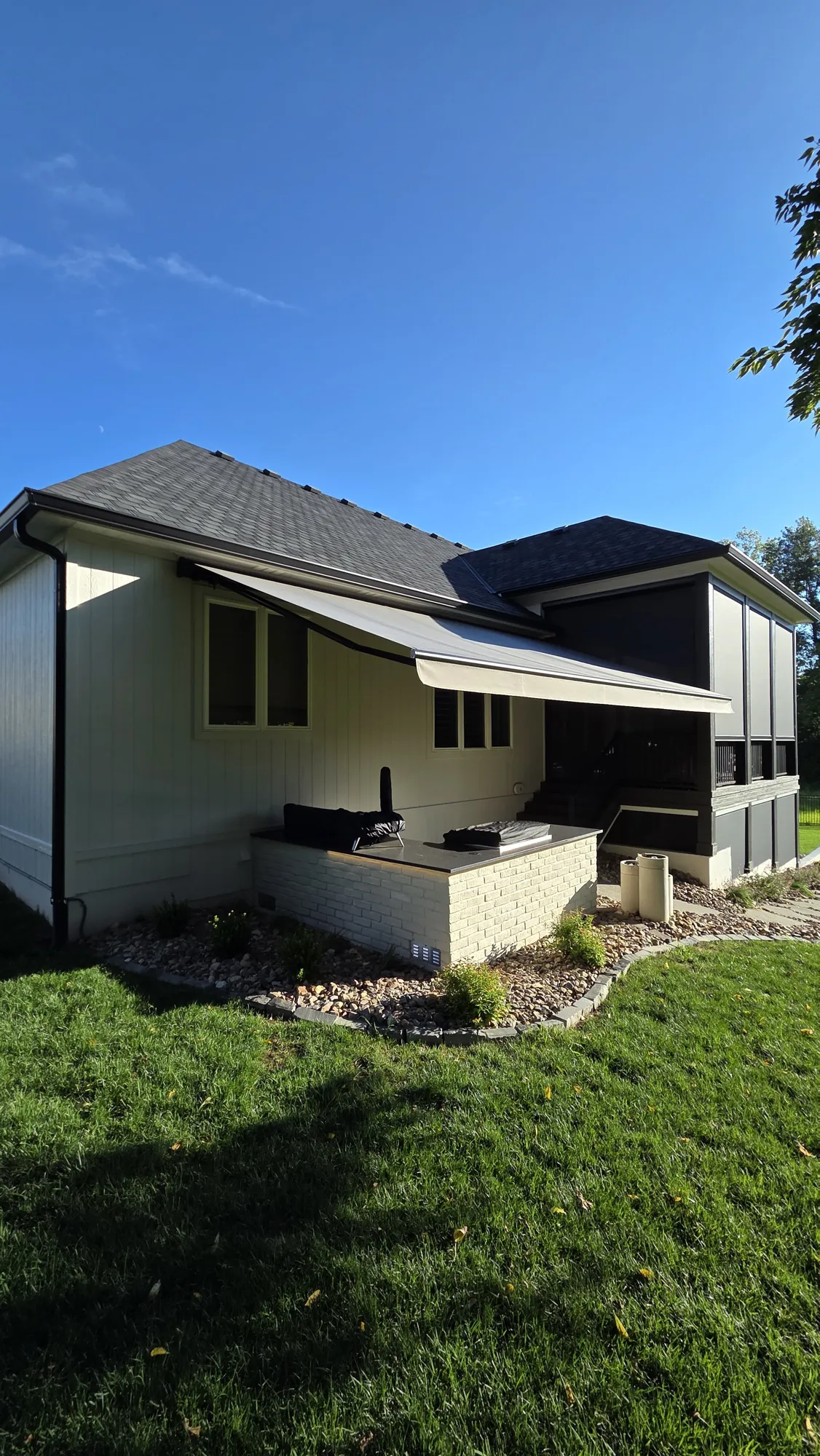 Retractable awning extended over an outdoor kitchen on a gray and white home, installed by Solar Shield Blinds