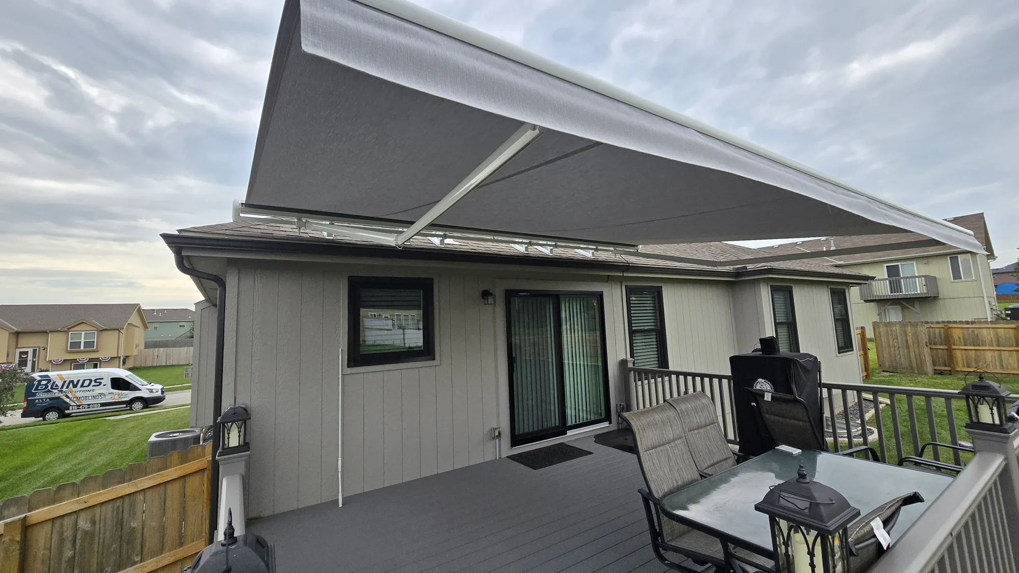Gray retractable awning extended over a deck with a dining set, installed by Solar Shield Blinds