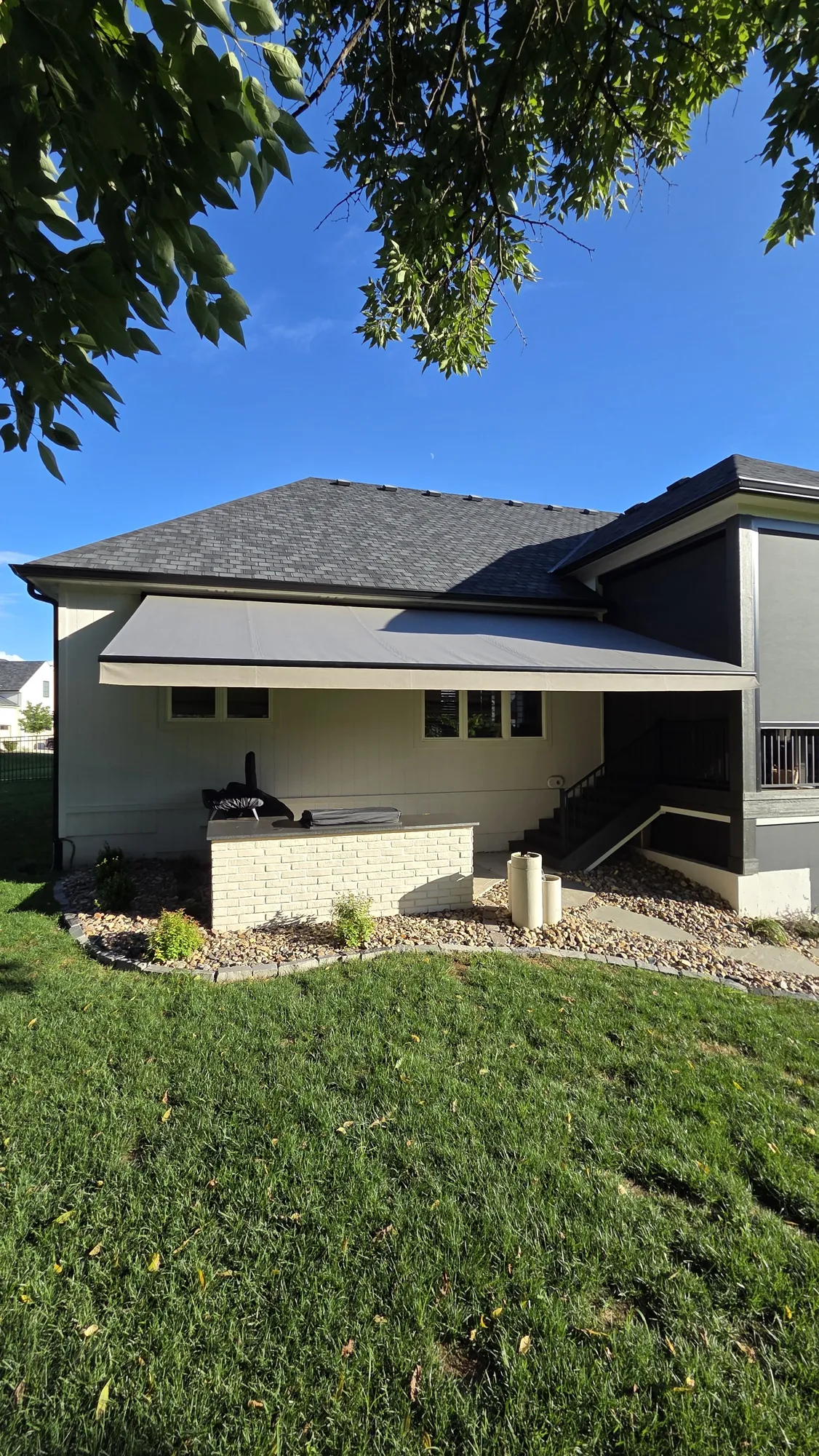 Retractable awning shading an outdoor kitchen and lower patio, installed by Solar Shield Blinds