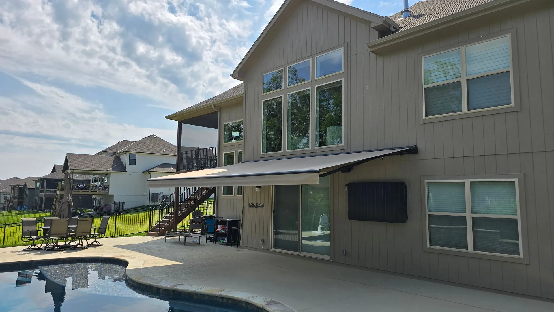 Retractable awning over the lower patio of a two story home beside a pool, installed by Solar Shield Blinds