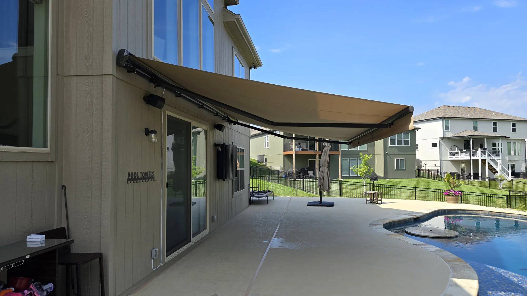 Tan retractable awning extended over a pool patio, installed by Solar Shield Blinds