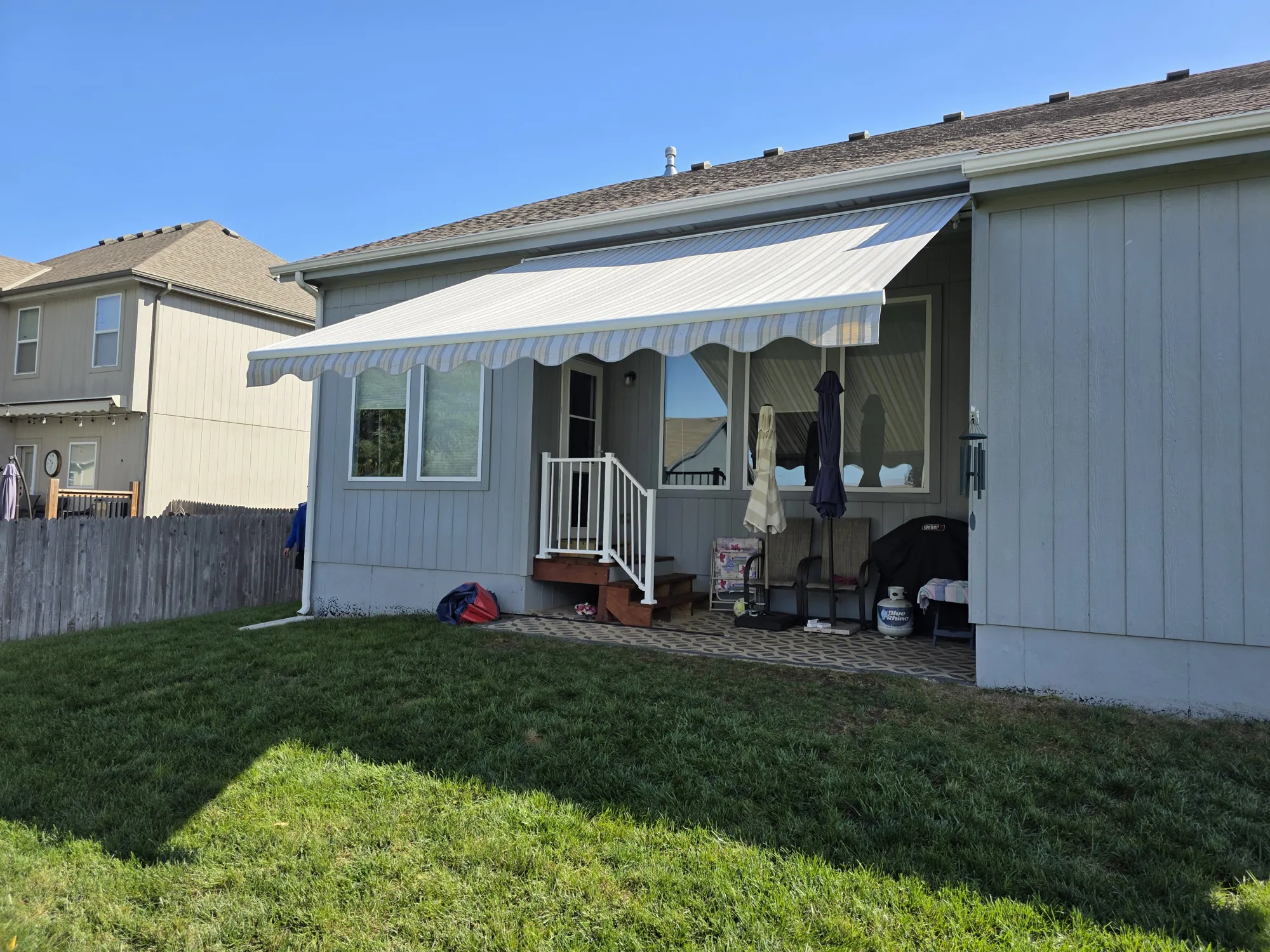 Striped retractable awning over the back patio of a gray sided home, installed by Solar Shield Blinds