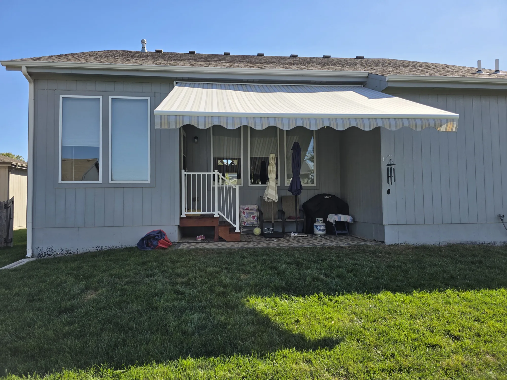 Striped retractable awning with a scalloped valance over a back patio, installed by Solar Shield Blinds