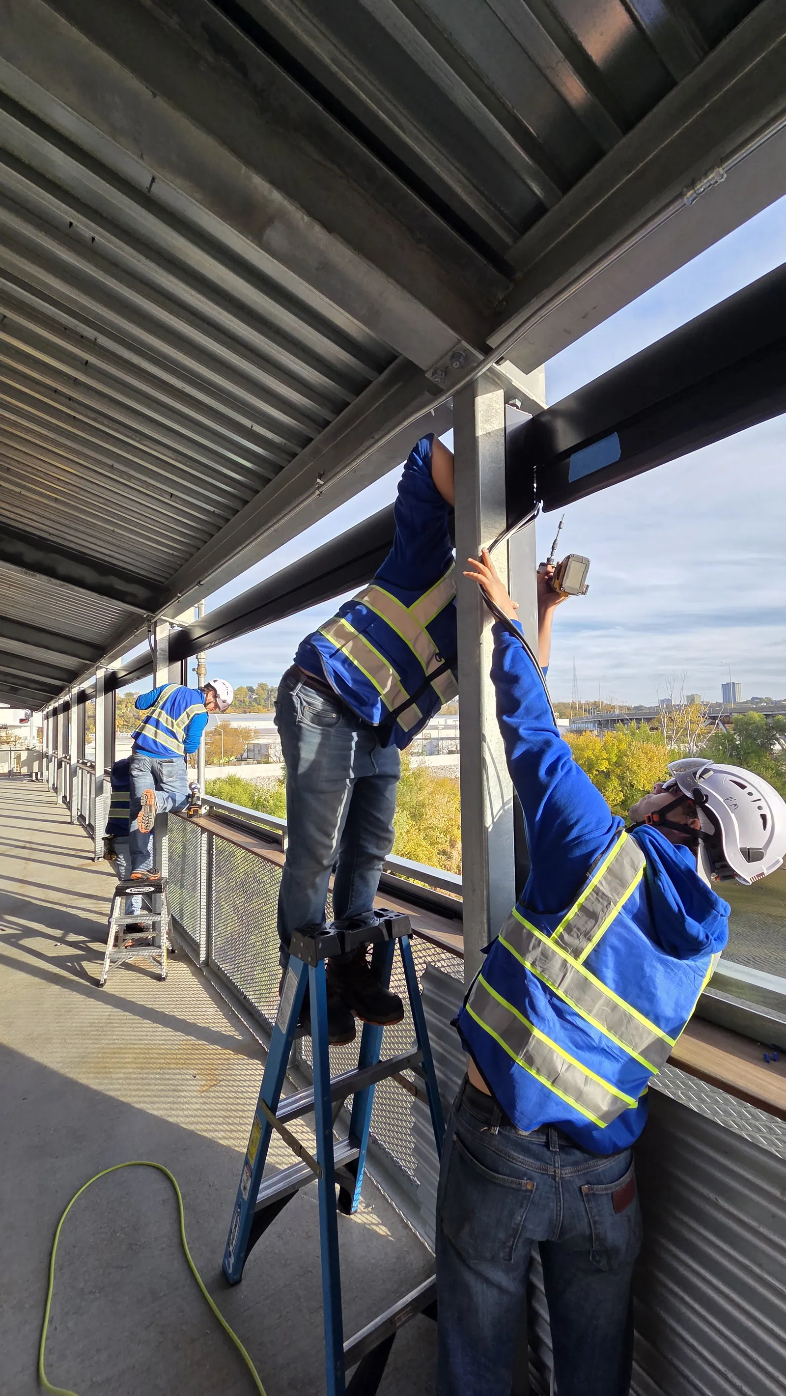 An installer setting a shade header into the bridge frame from a step ladder