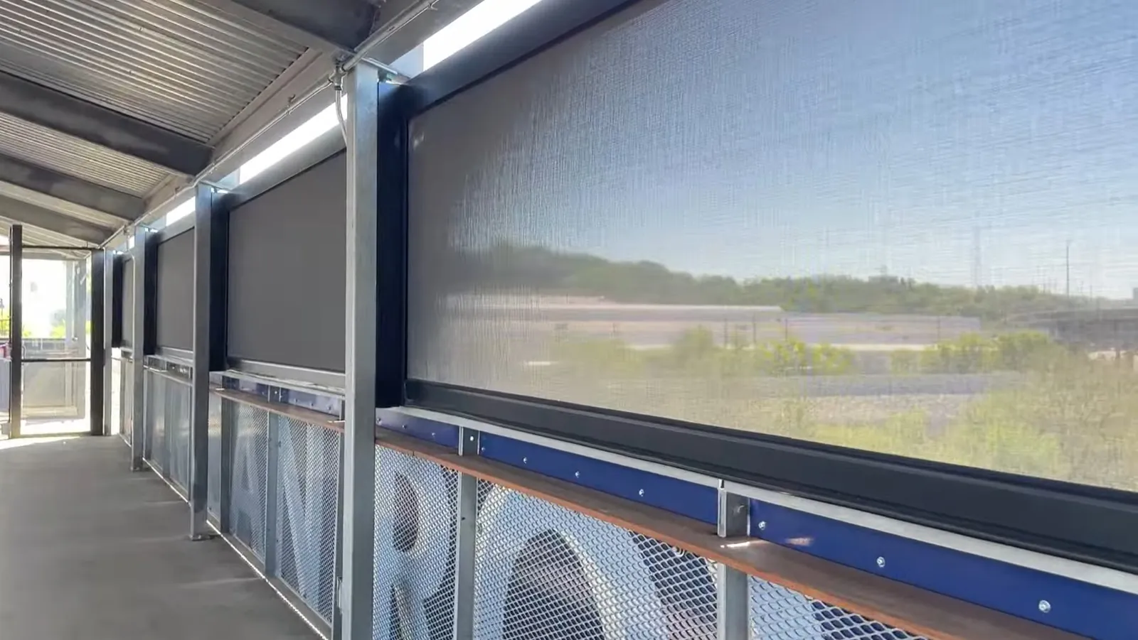 Motorized exterior screens lowered along the Rock Island Bridge walkway, the river showing through the mesh