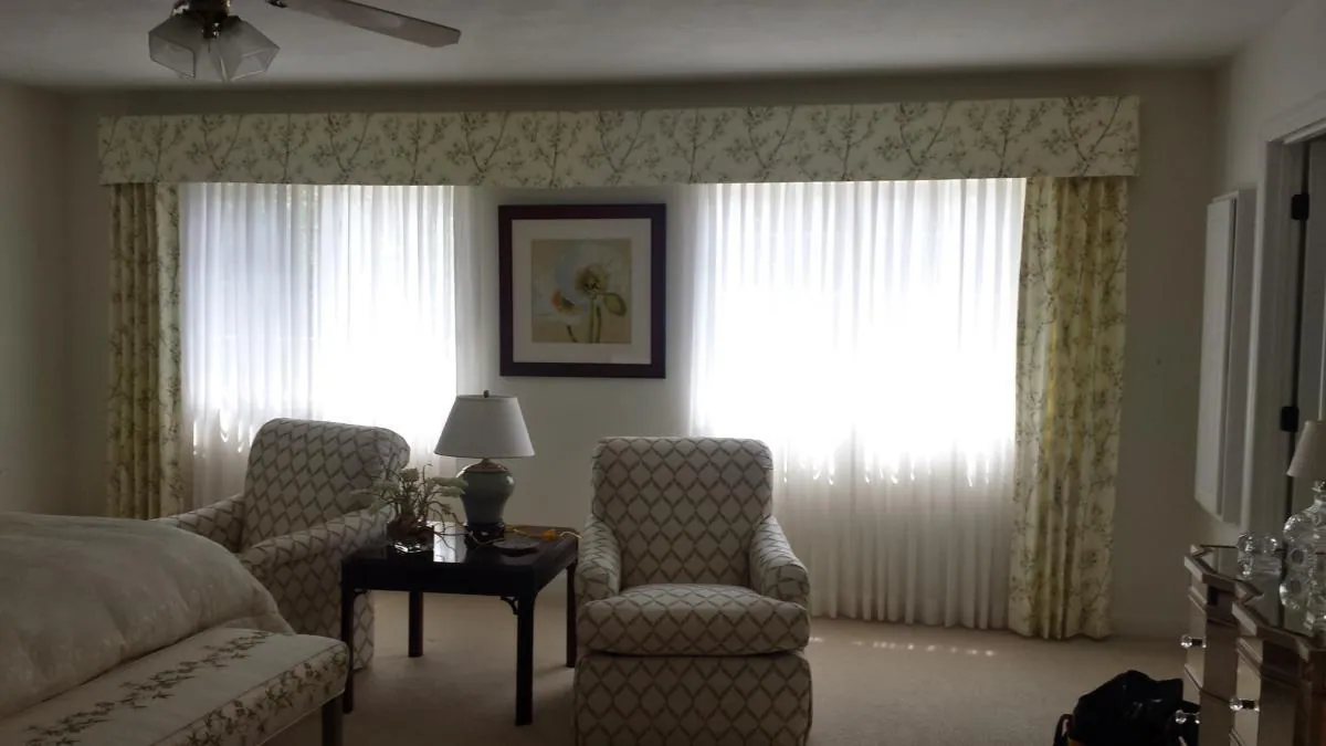 Sheer panels and a patterned top treatment across a sitting room window wall, installed by Solar Shield Blinds