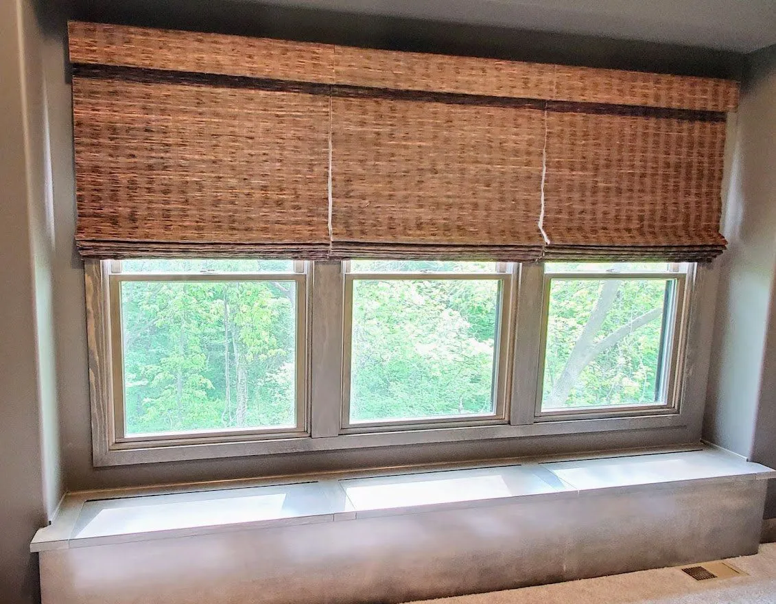 Natural woven shade over three windows above a window seat