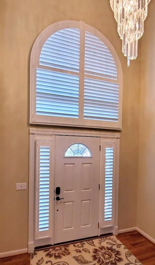 White plantation shutters on an arched window above a front door and its sidelights