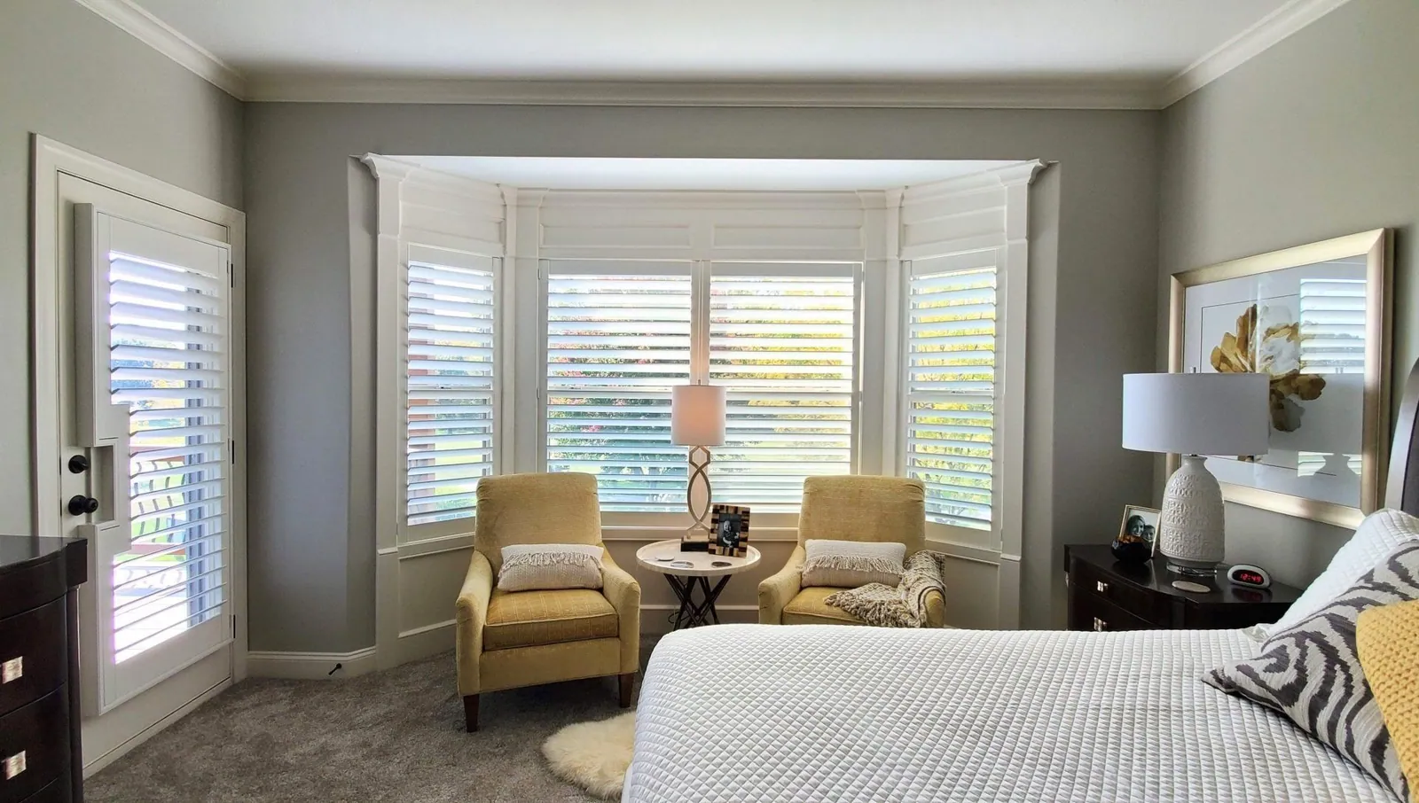 White plantation shutters on a bay window and a door in a bedroom
