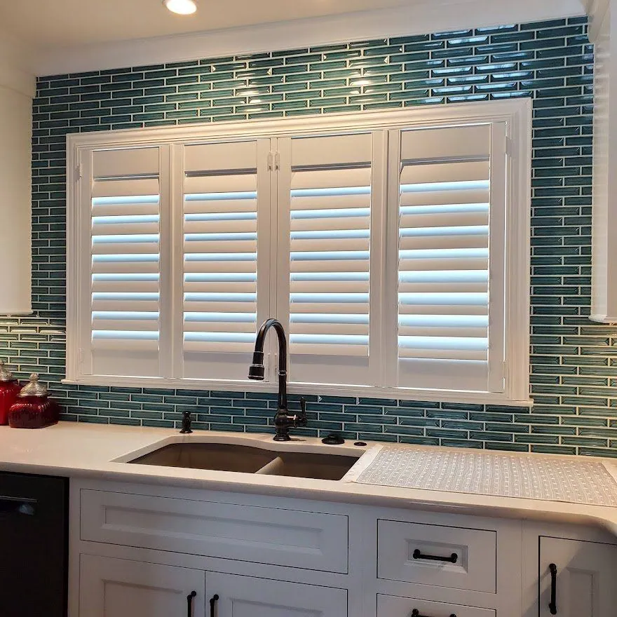 White plantation shutters over a kitchen sink with a tile backsplash