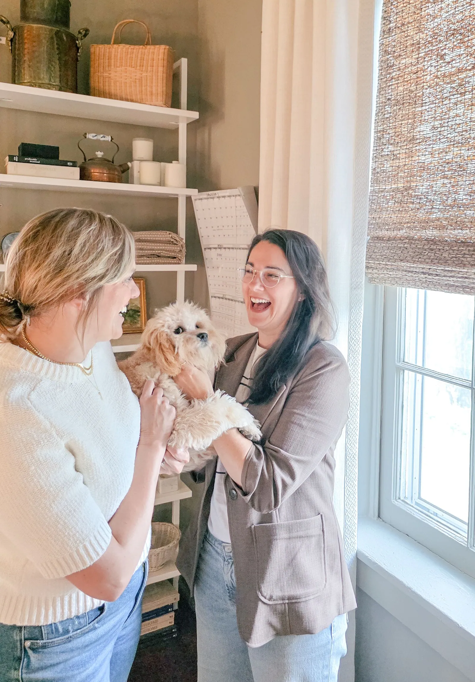 Two designers laughing together with a small dog beside a woven shade