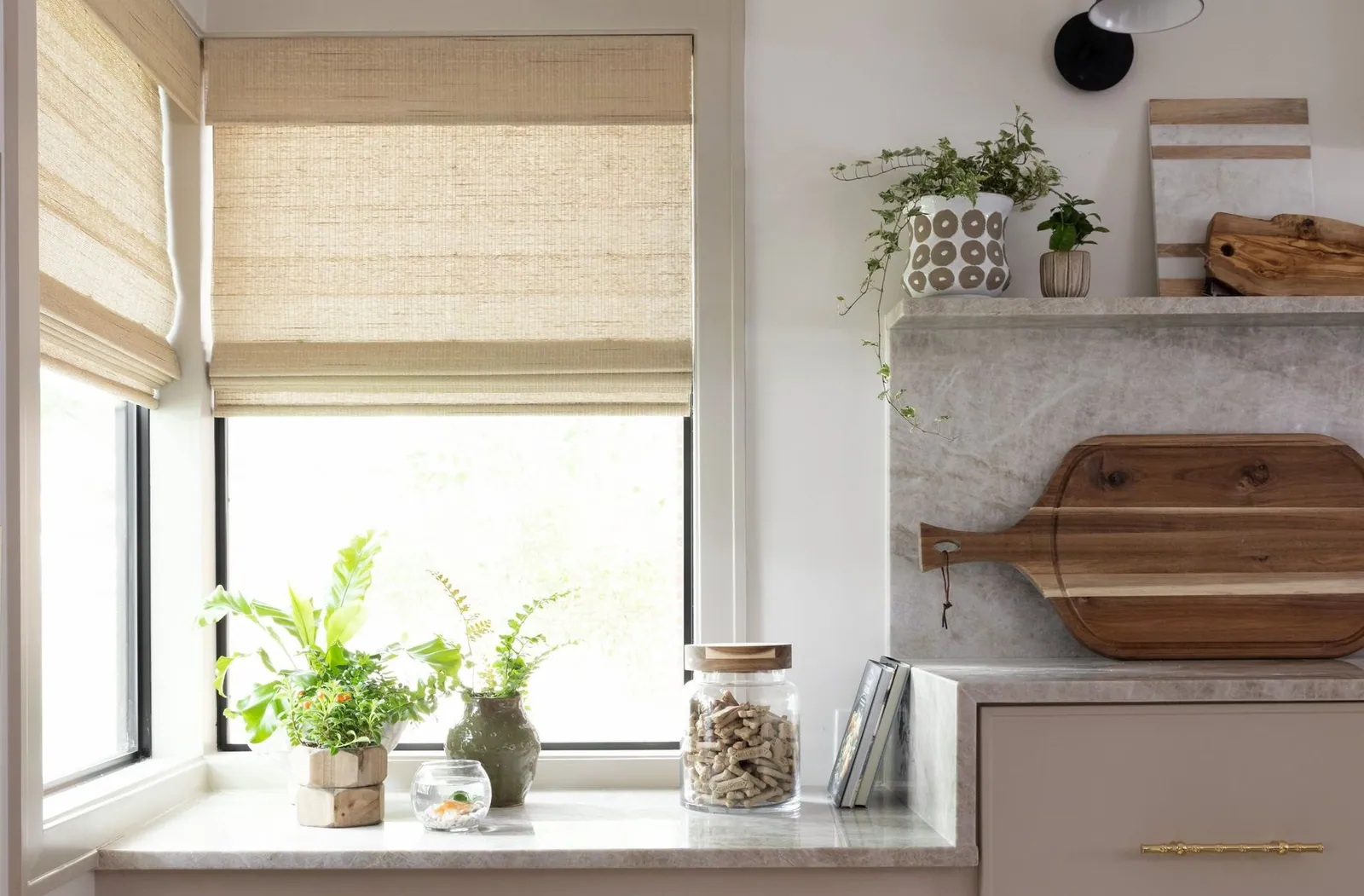 Natural woven shades on kitchen windows above a counter with plants, installed by Solar Shield Blinds
