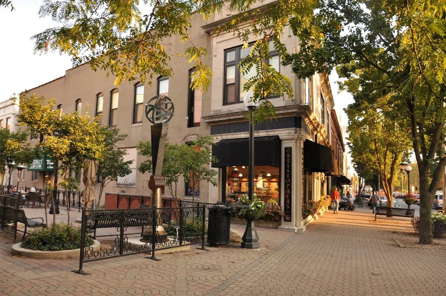 A downtown street corner with a street clock, shopfronts and trees
